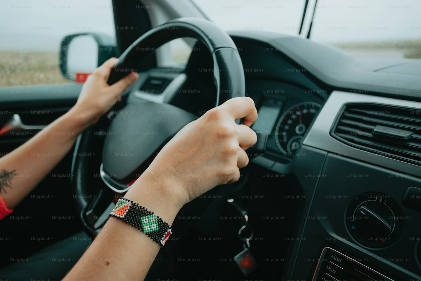 Driver with a beaded bracelet gripping the steering wheel with both hands