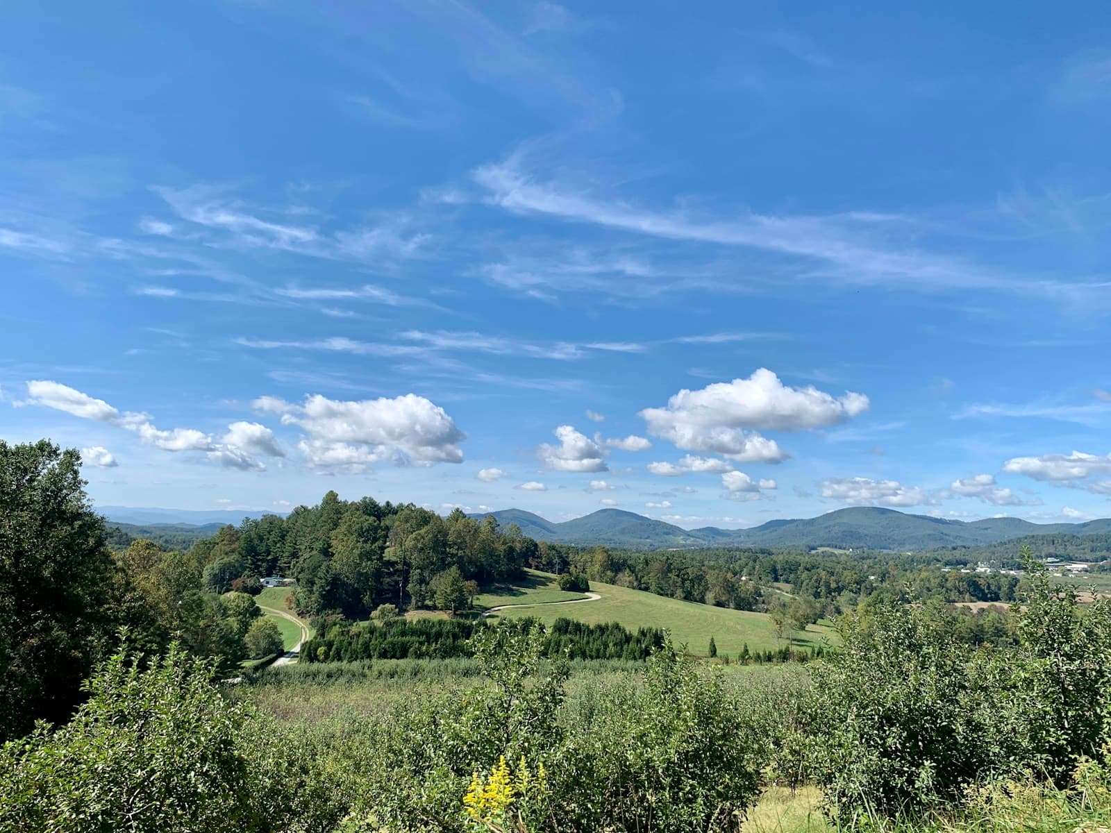 Panoramic view of green rolling hills, farmland, and distant mountains under a blue sky with white clouds