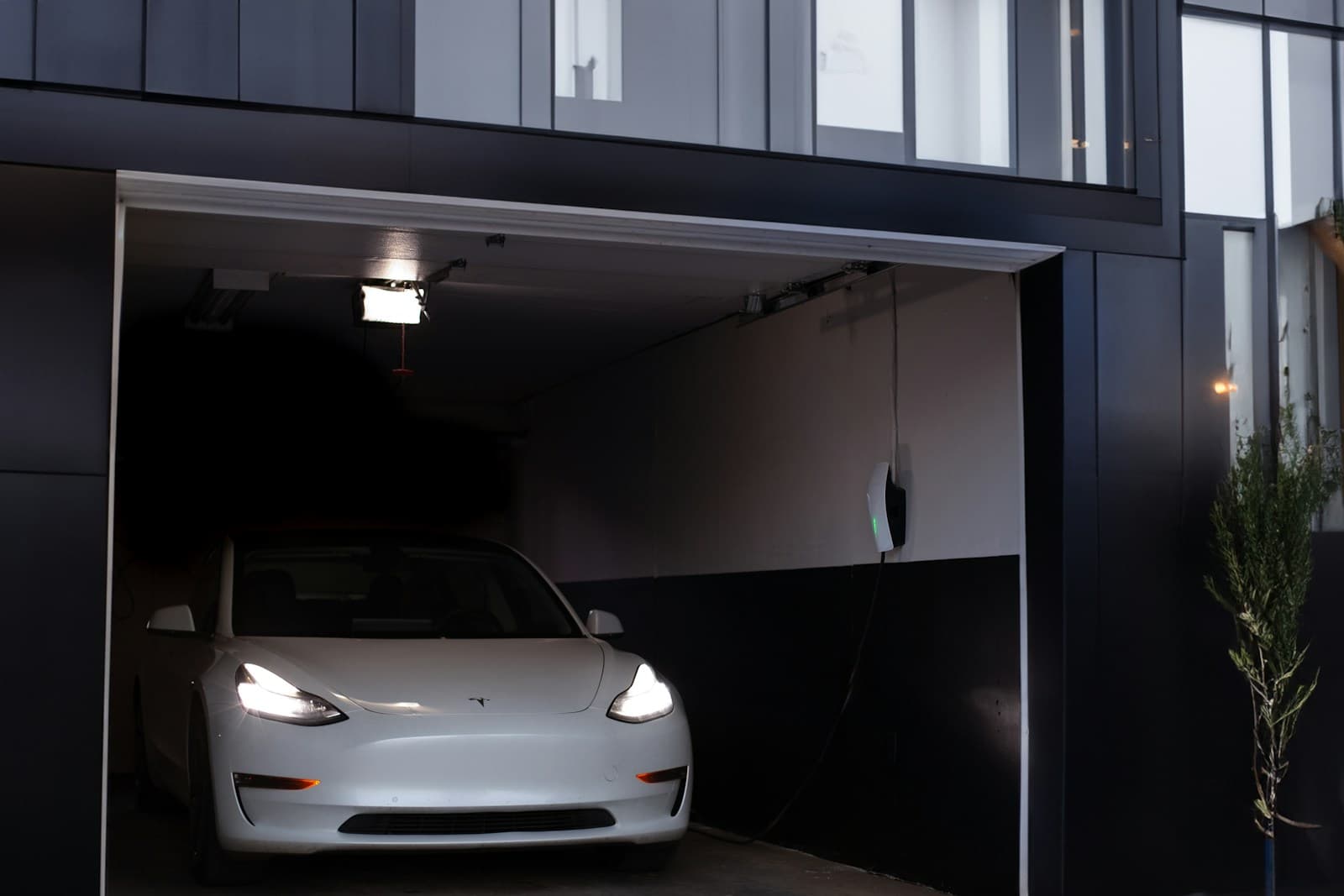 White Tesla Model 3 parked in a modern home garage with its headlights on