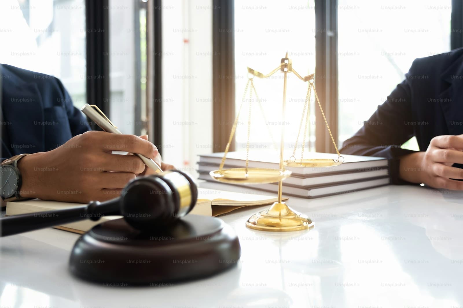 Legal consultation with gavel, scales of justice, and law books on desk between lawyer and client