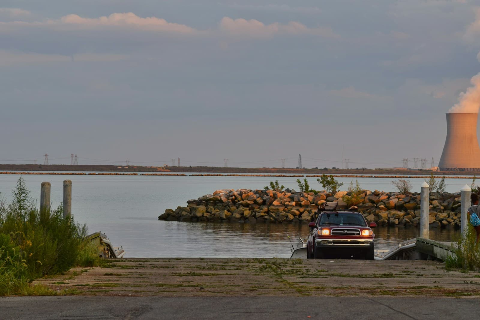 Car parked at waterfront boat ramp with nuclear power plant cooling tower visible across the water
