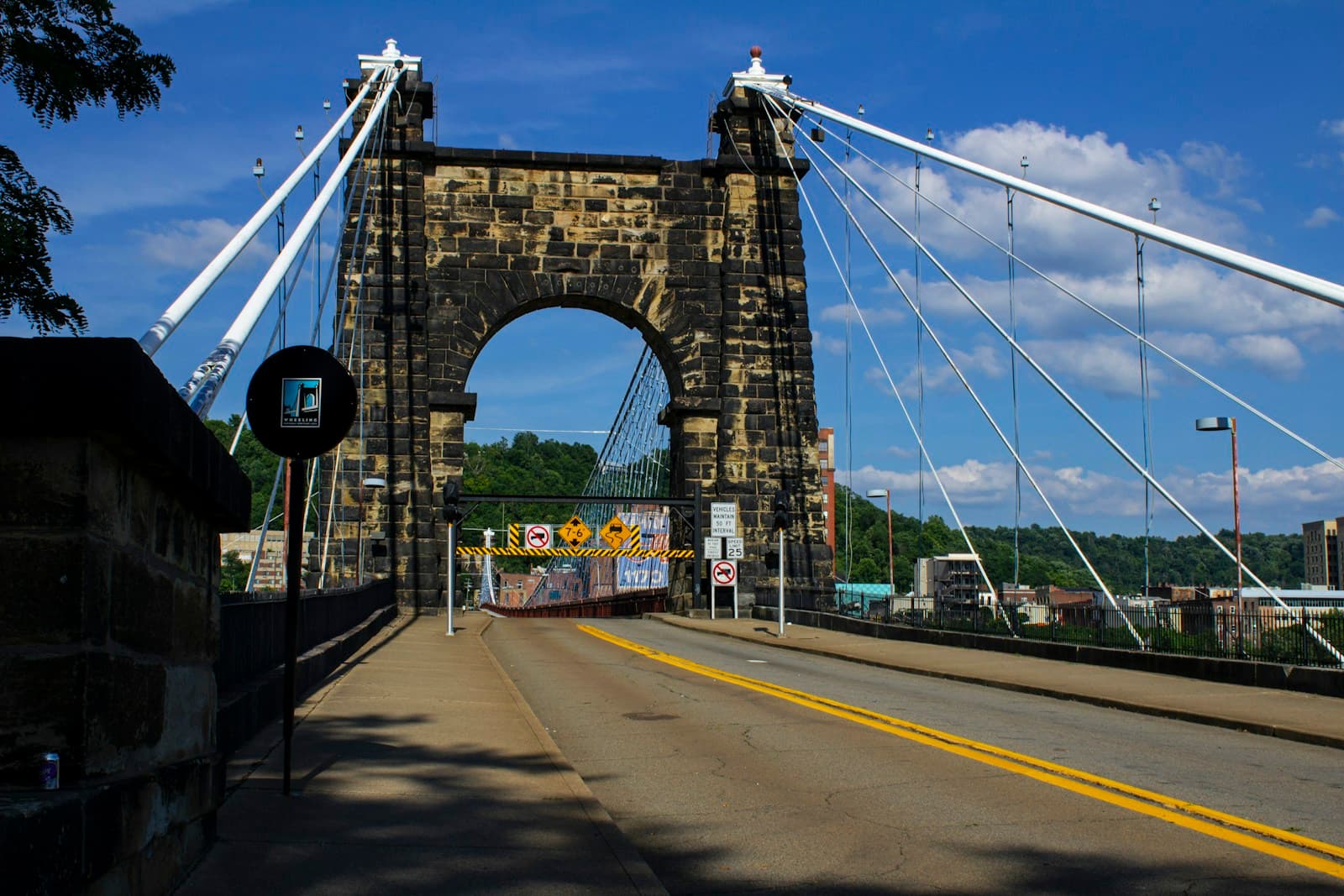 Historic stone suspension bridge with twin towers and white cables spanning a road under blue sky