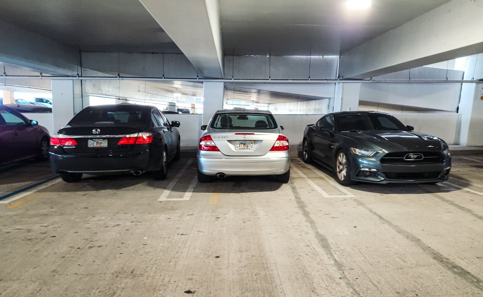 Three cars parked in an underground parking garage with concrete floors and fluorescent lighting