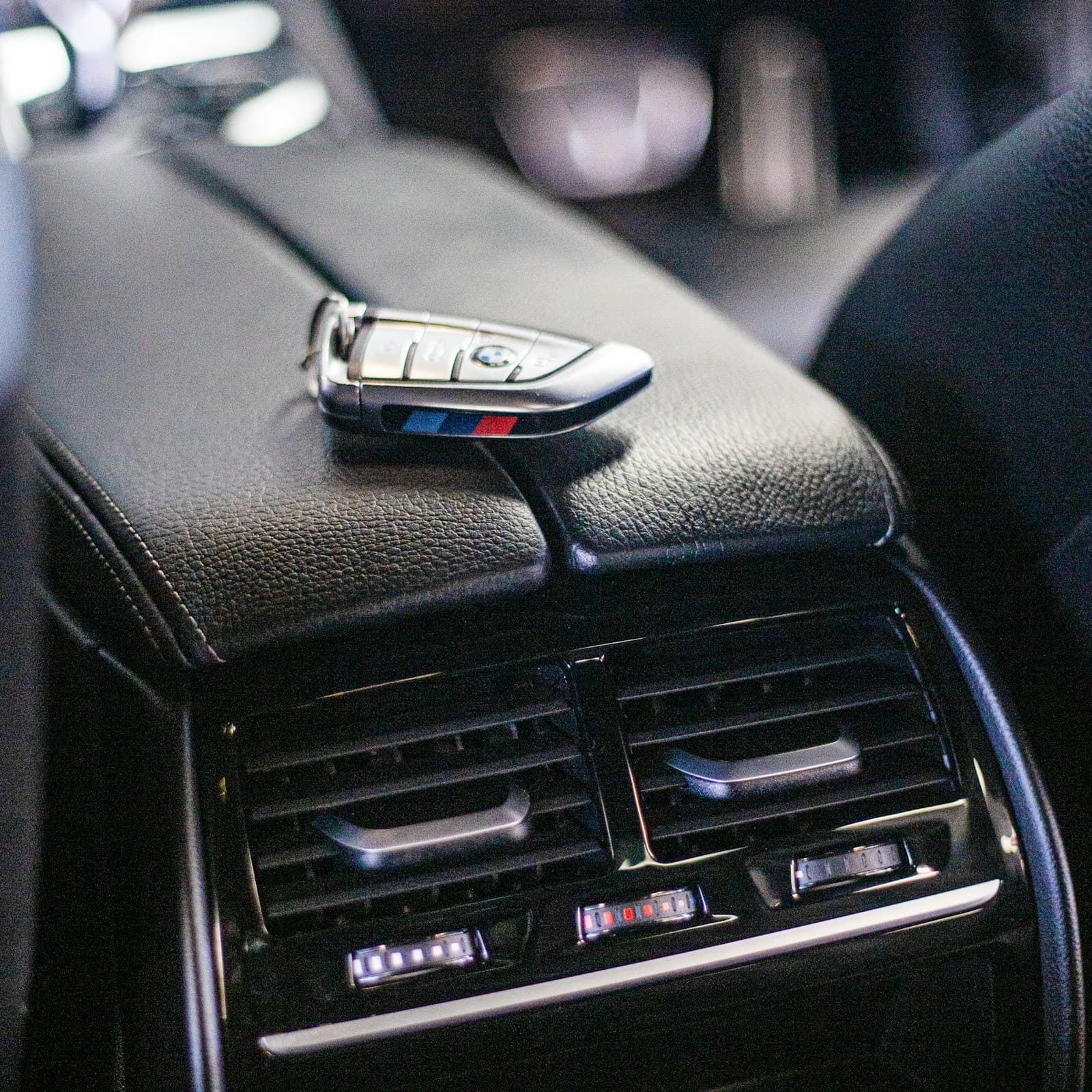 BMW car key fob sitting on black leather interior near air vents in luxury vehicle