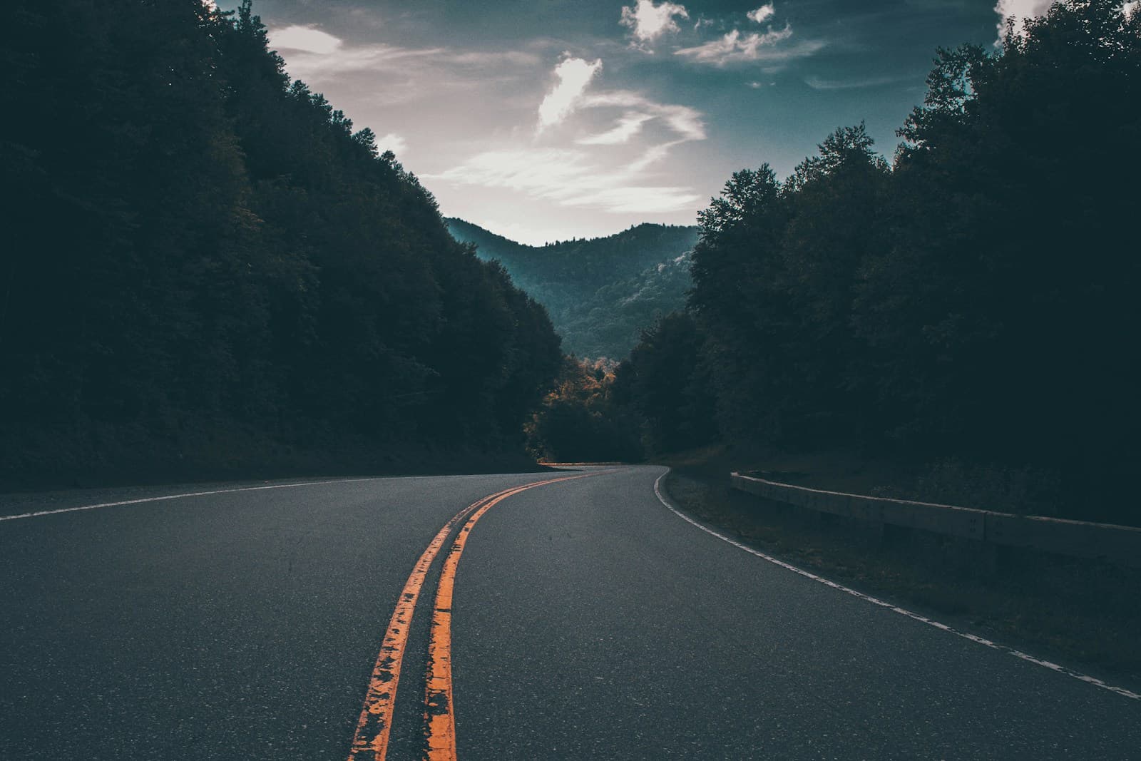Empty road with yellow double lines curving through a forested valley