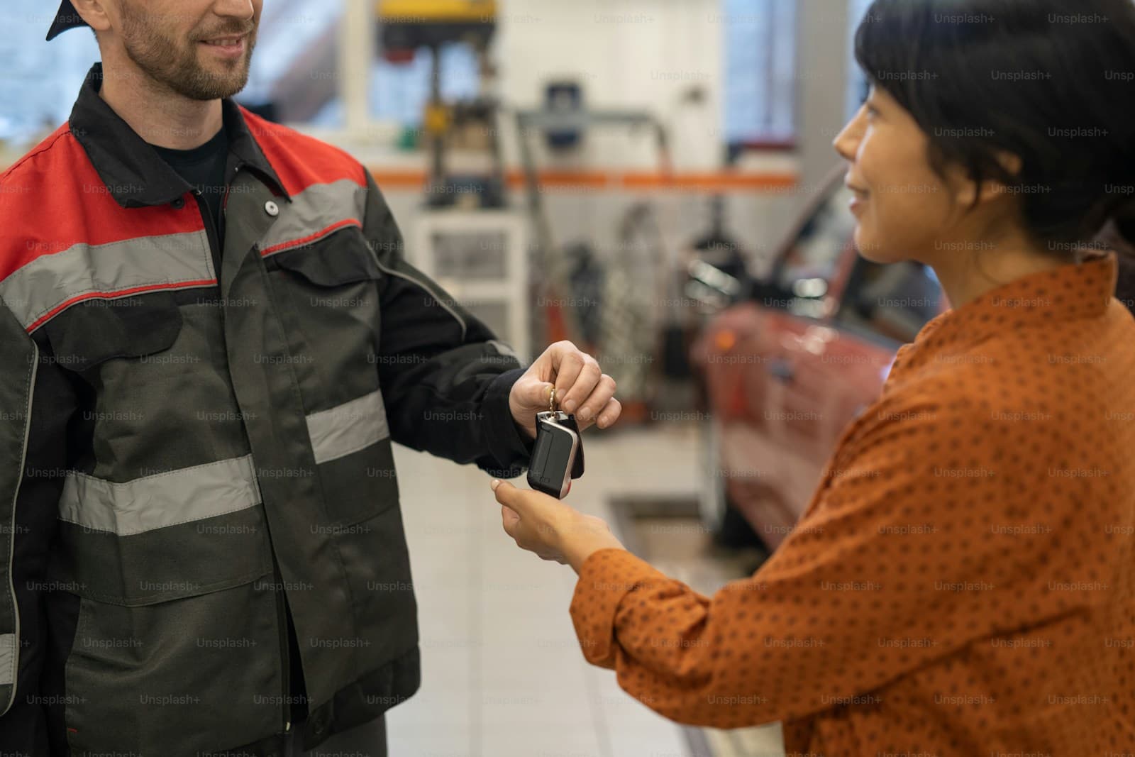 Mechanic in work coveralls handing keys to customer in orange sweater at automotive service center