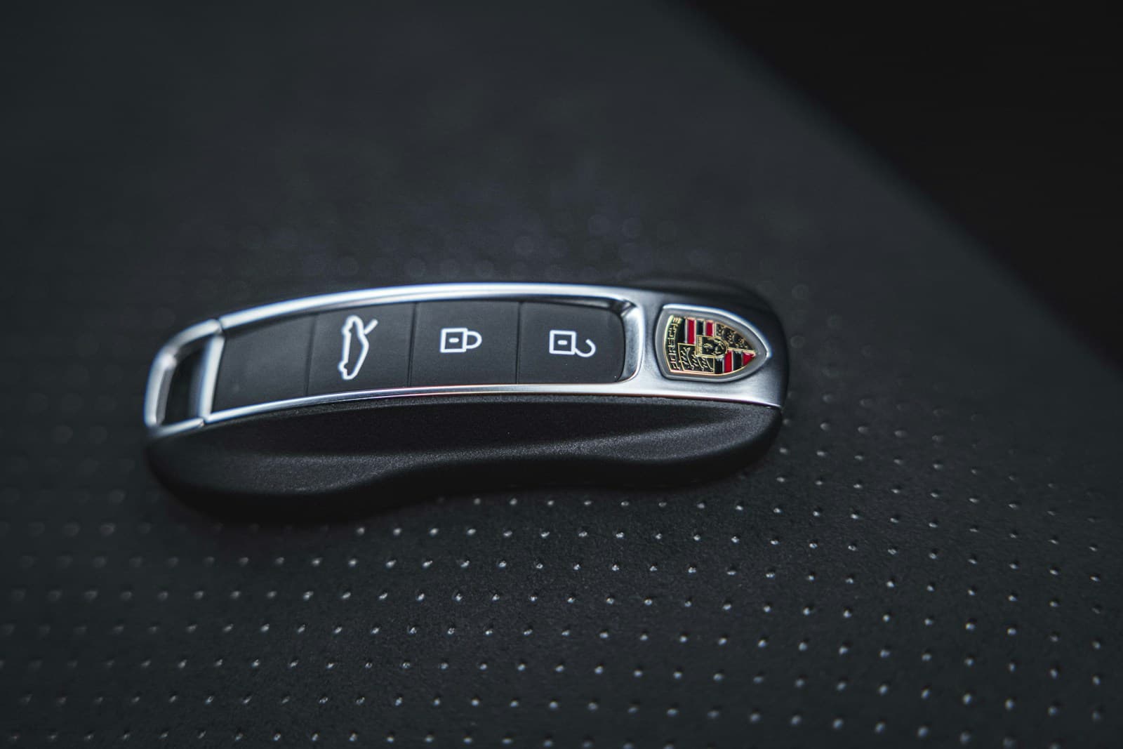 Black Porsche key fob with chrome accents and control buttons on textured dark surface