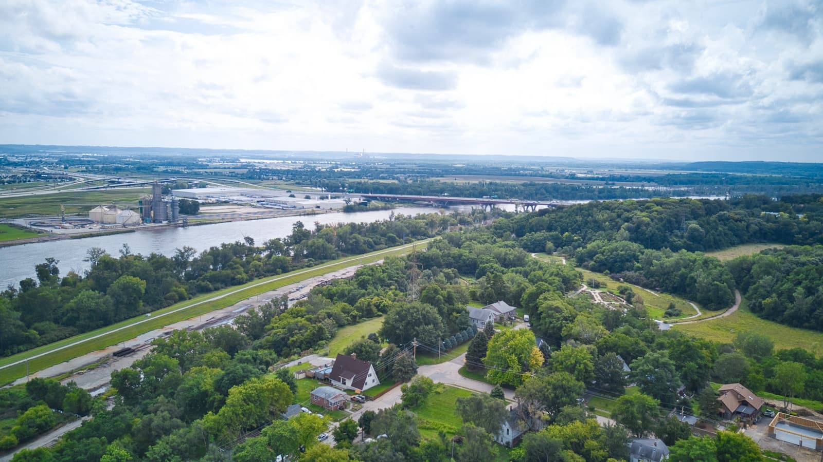 Aerial view of suburban neighborhoods surrounded by green forests with highway and water in background