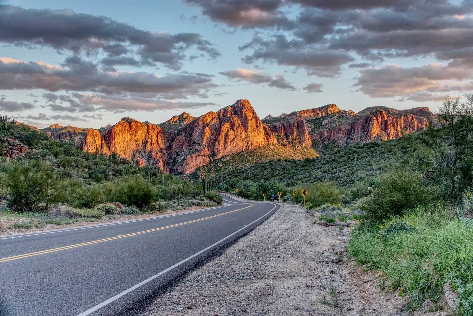 Desert highway leading toward red rock cliffs at sunset in southwestern landscape