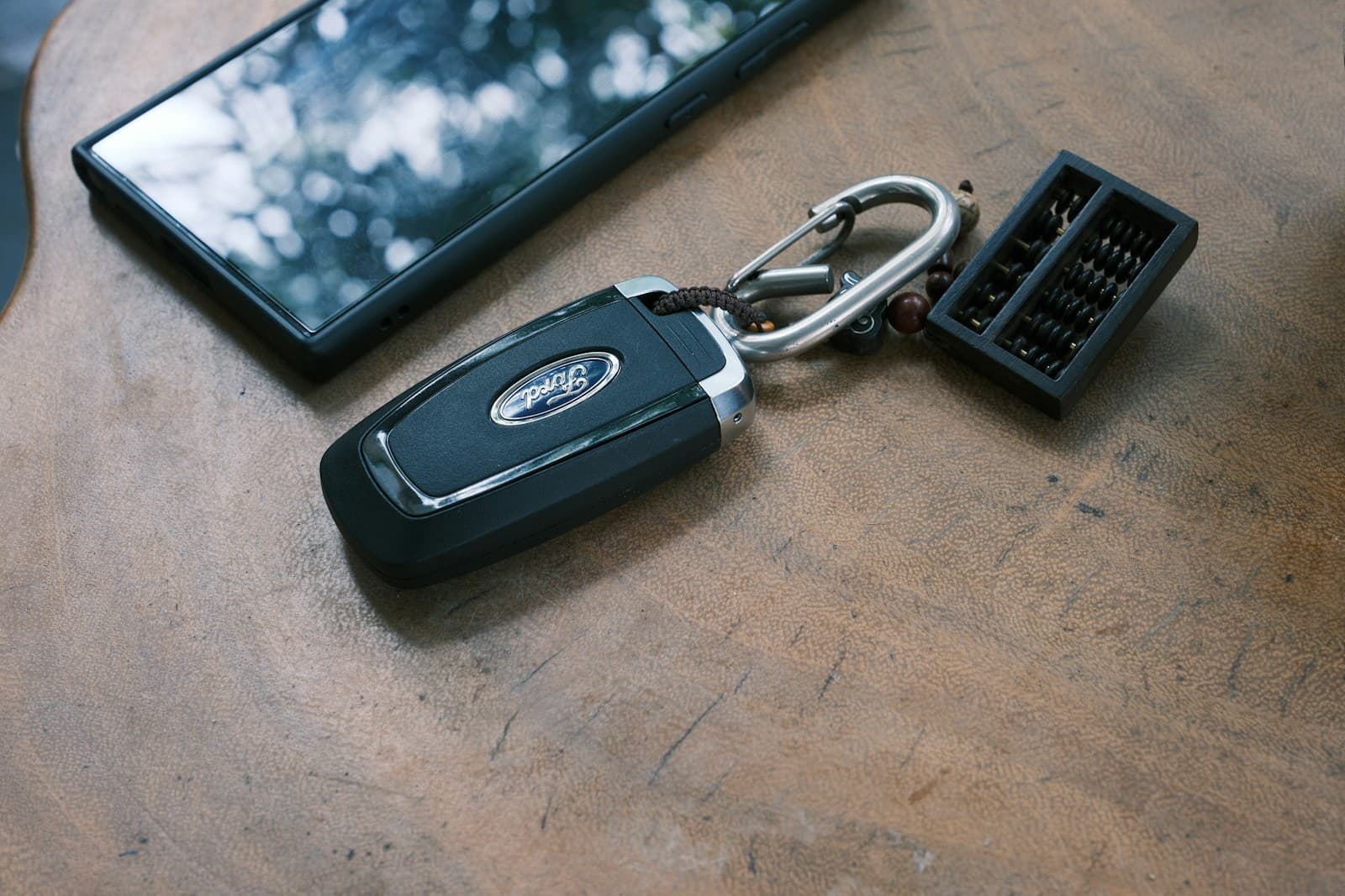 Black Ford car key fob with keychain on wooden table next to smartphone and small electronic device