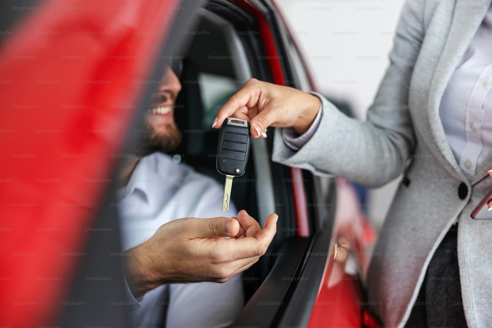 Salesperson in a gray suit handing car keys to a buyer seated in a red car