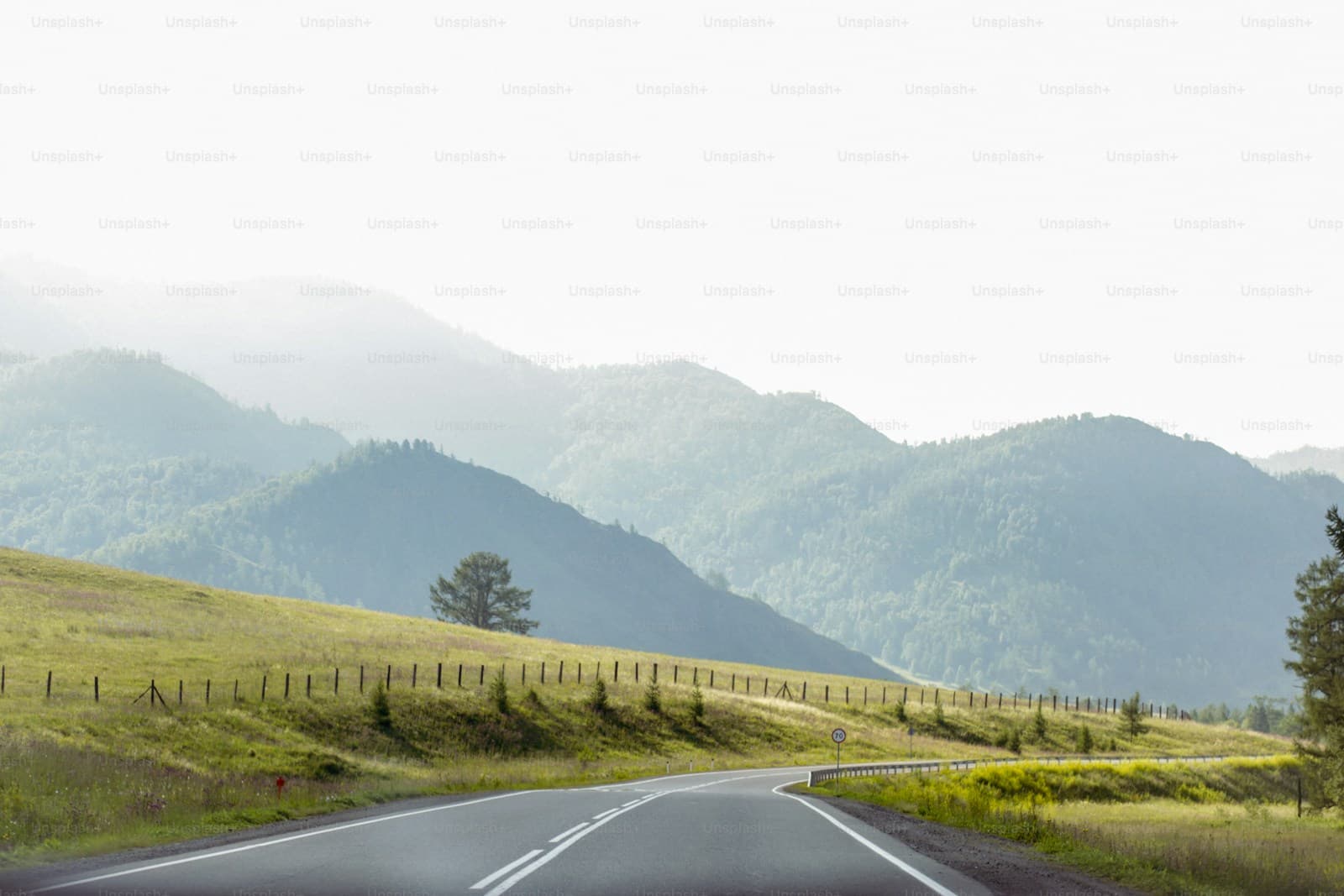 Highway crossing rolling green hills with layers of misty mountains beyond