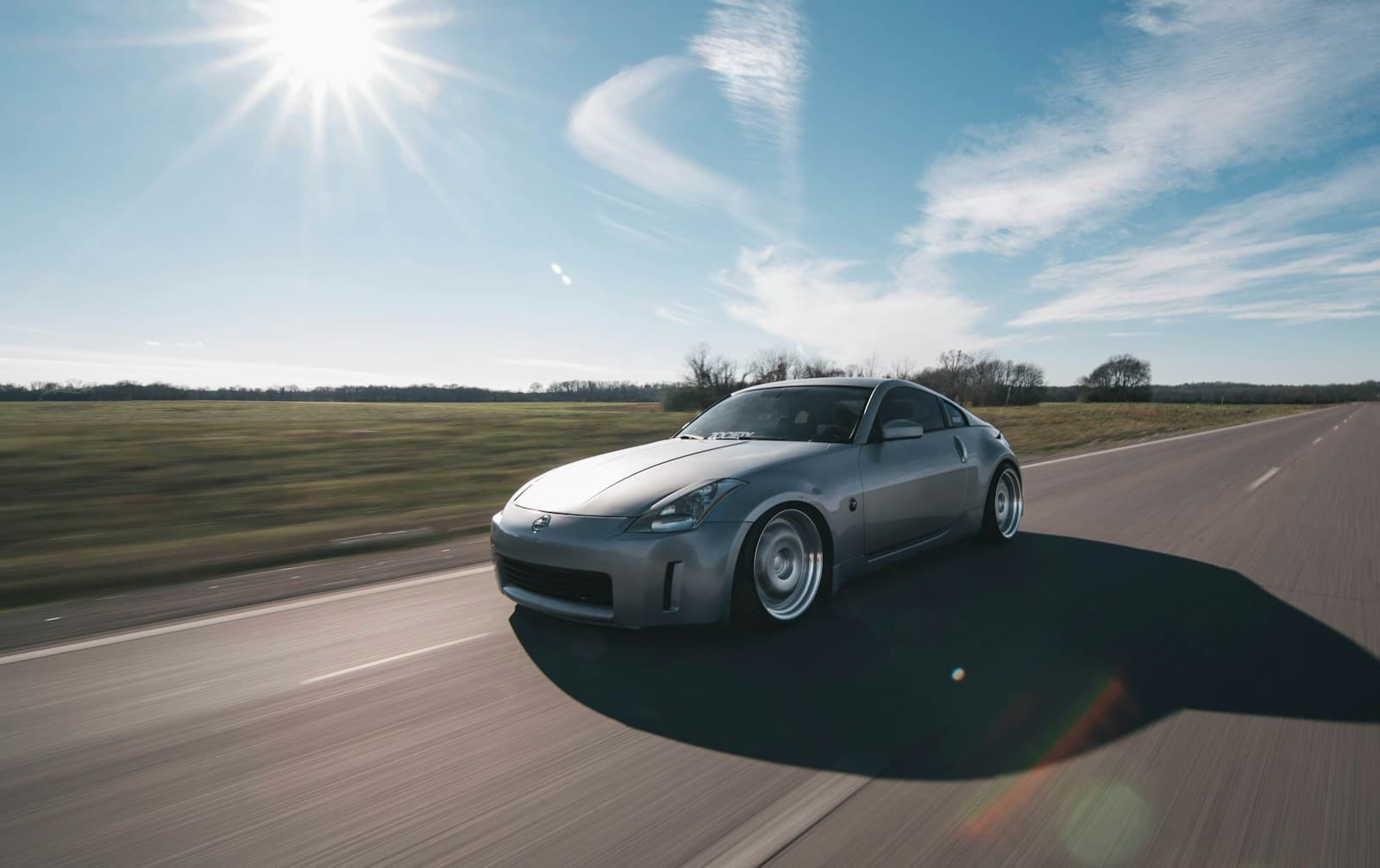 Silver sports car driving on empty road with motion blur under bright sunny sky