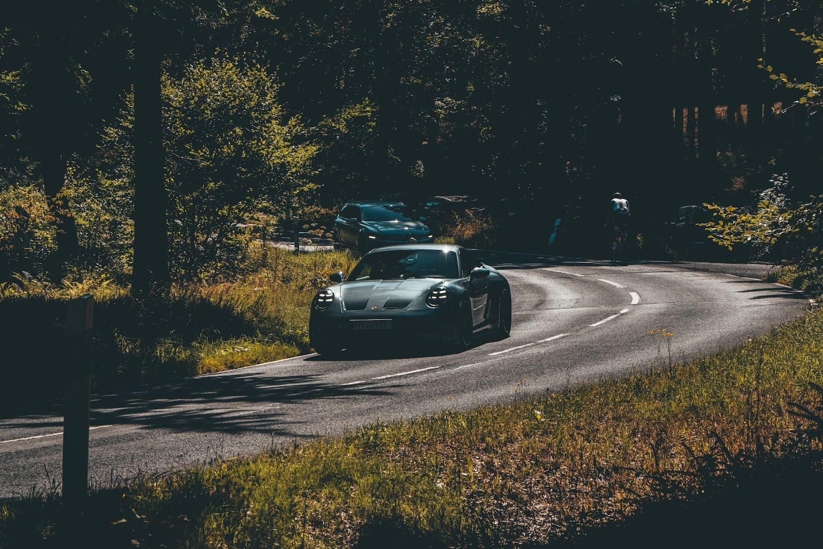 Sports car driving on winding road through autumn forest with golden sunlight
