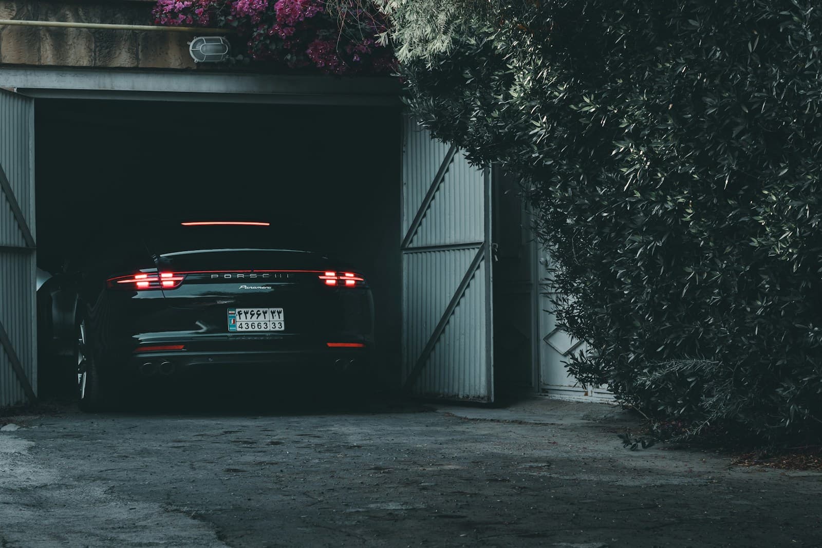 Dark car pulling into a garage with open wooden doors surrounded by greenery