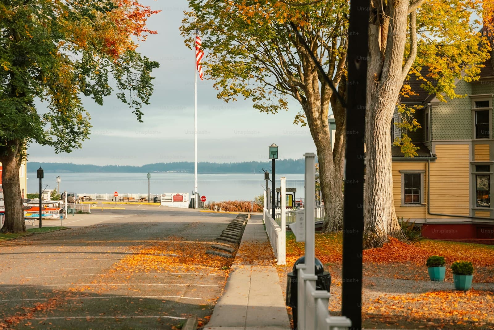 Autumn street scene with colorful fall trees, sidewalk, building, and water view in background