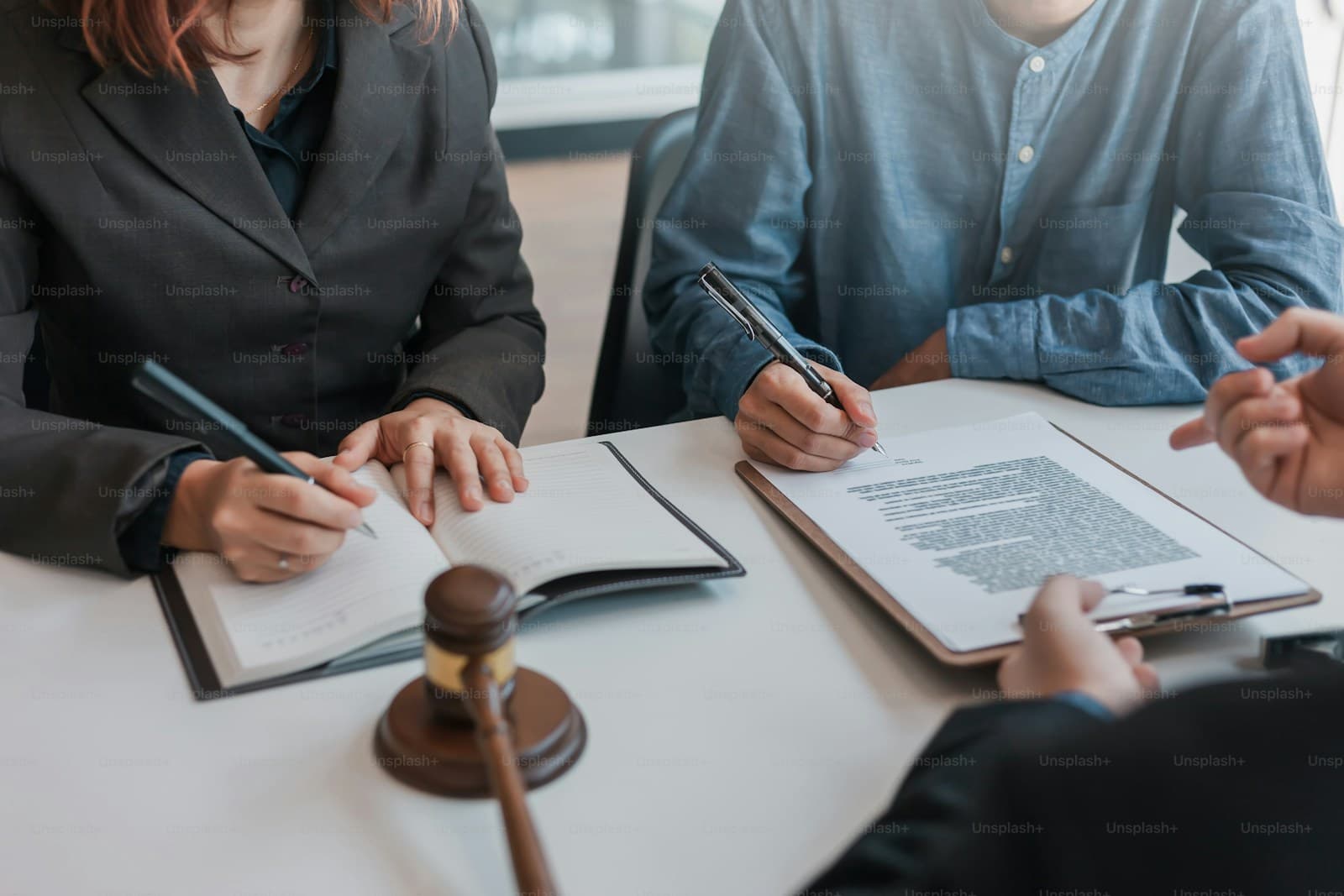 Three people signing documents at a table beside a wooden gavel