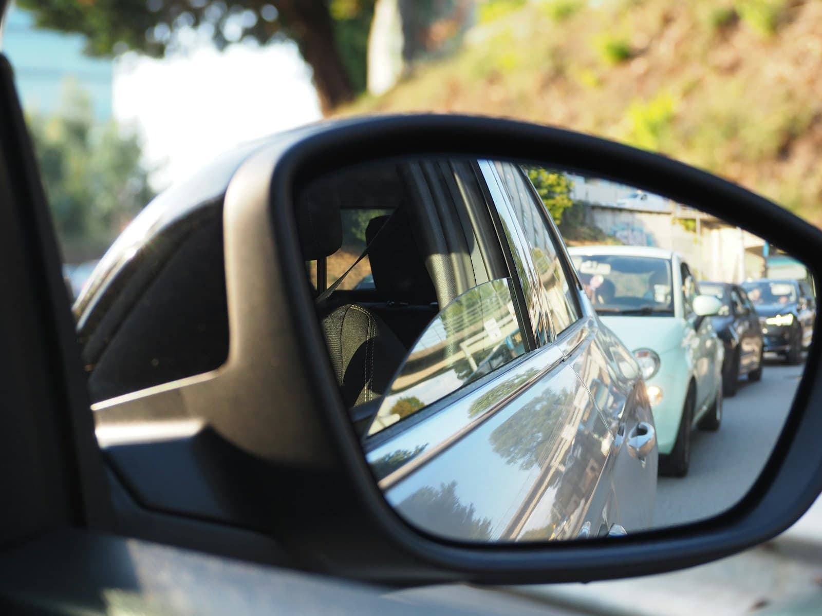Car side mirror reflecting traffic and vehicles behind on a sunny street