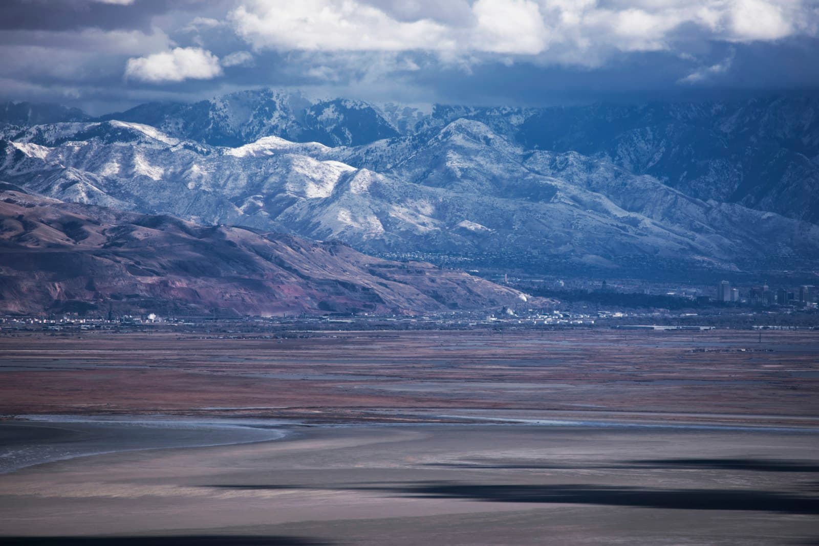 Snow-capped mountains behind a reflective salt flat under dramatic cloudy sky in desert landscape